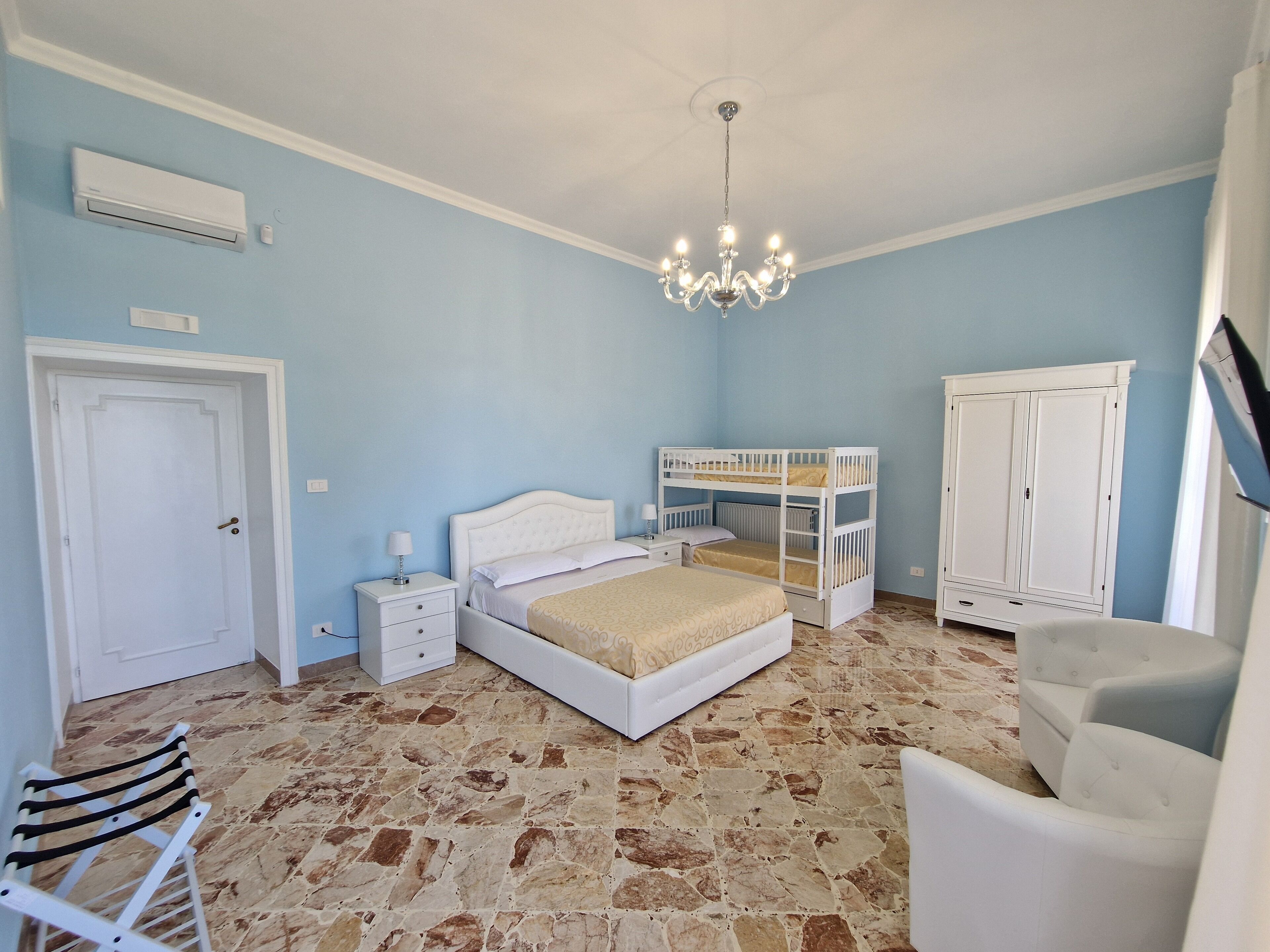Un dormitorio con una cama litera, un armario blanco, una mesita de noche con lámpara y una silla.
