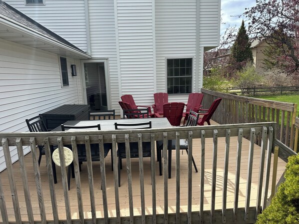 Een terras met een tafel, stoelen, een kleine barbecue en uitzicht op een wit huis.