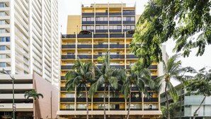 Un hotel de varios pisos con balcones, palmeras y un aparcamiento.