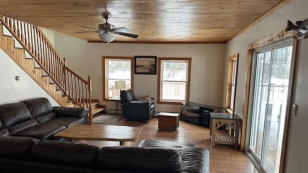 A spacious living room with a wooden ceiling, a black leather sofa, a wooden coffee table, and a black armchair. There is a staircase with wooden railings leading to another level.