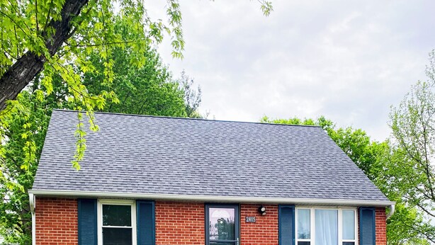 A two-story house with a brick exterior, a dark roof, and a front yard with a stone retaining wall and a small garden. - Cozy home in St. Joseph, MO that is centrally located to hospital & university! (Saint Joseph)
