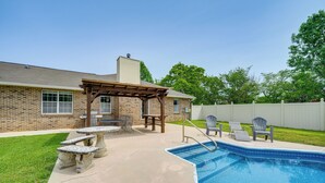 A backyard with a swimming pool, a pergola, outdoor furniture, and a brick house. - Perry Family Home on 2 Acres w/ Private Pool (Perry)