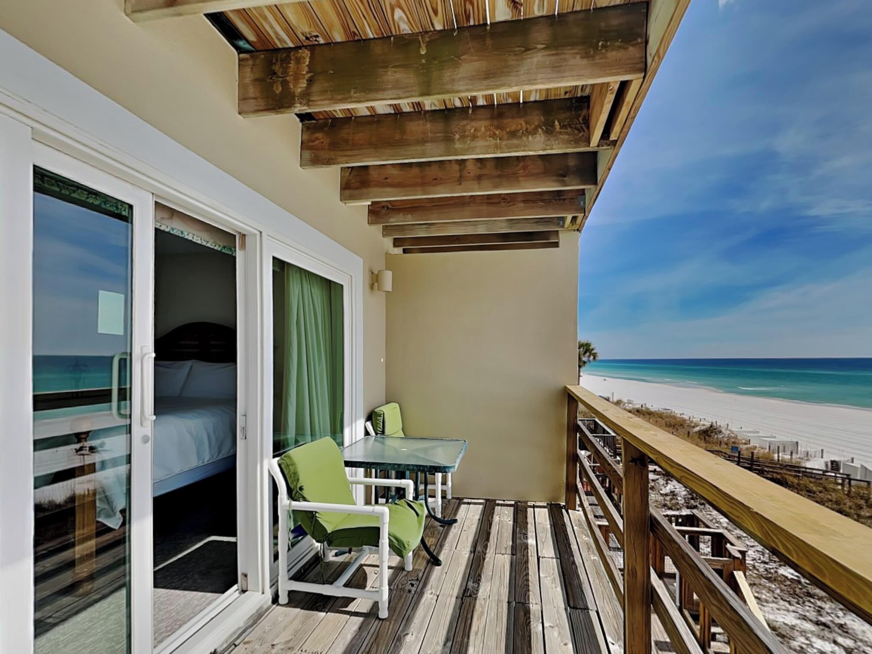 Un balcon doté d’une terrasse en bois, d’une table en verre et d’une chaise, offrant une vue sur la plage.