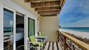A balcony with a wooden deck, a glass table, and a chair, overlooking a beach. - Anchor Townhome #5 by Southern Vacation Rentals (Destin)
