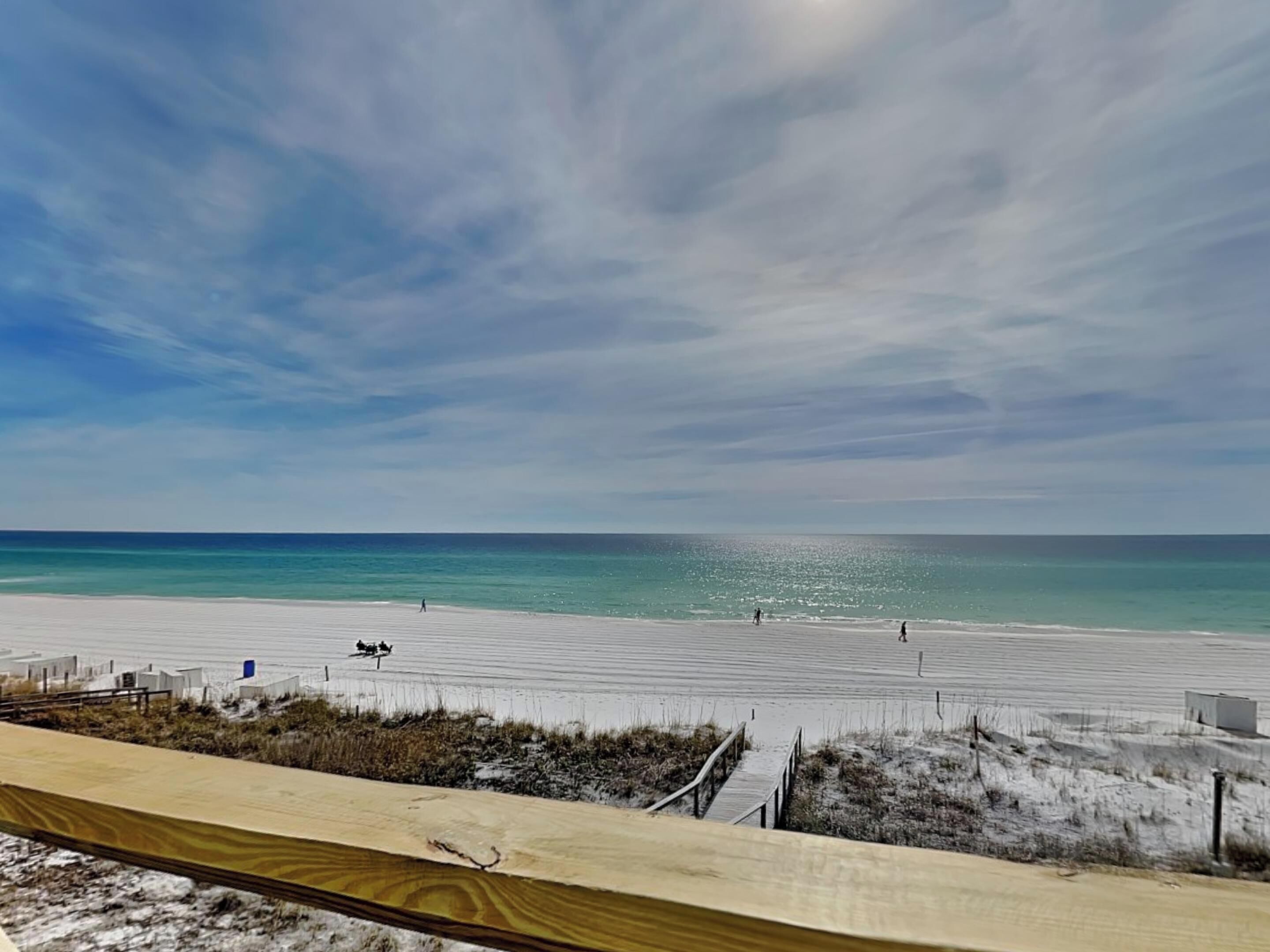 A beach with a wooden boardwalk leading to the water, a sandy beach, and a clear sky.