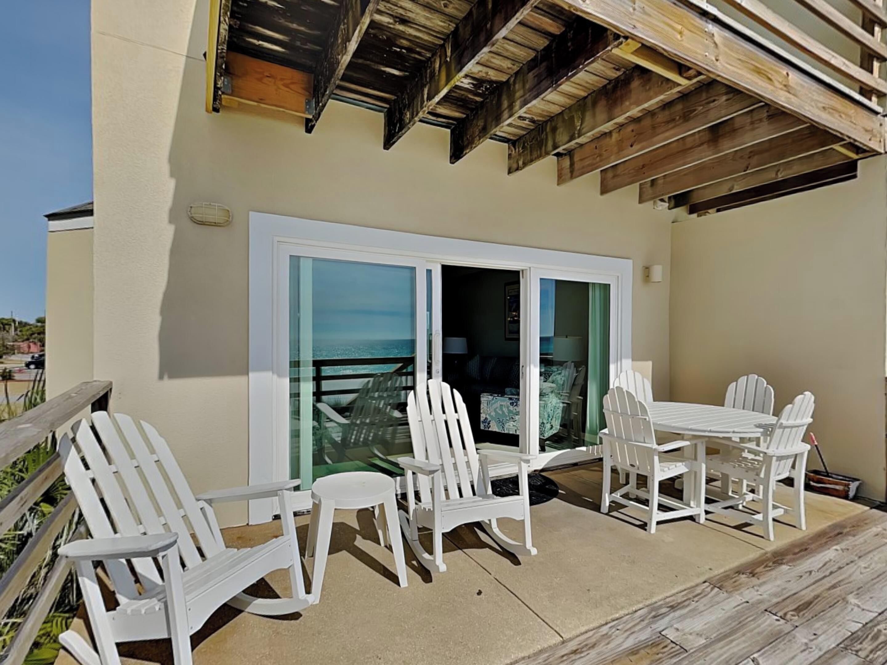 A patio with white chairs and a table, a sliding glass door, and a view of the ocean.