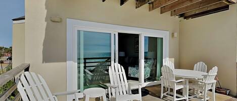 A patio with white chairs and a table, a sliding glass door, and a view of the ocean.