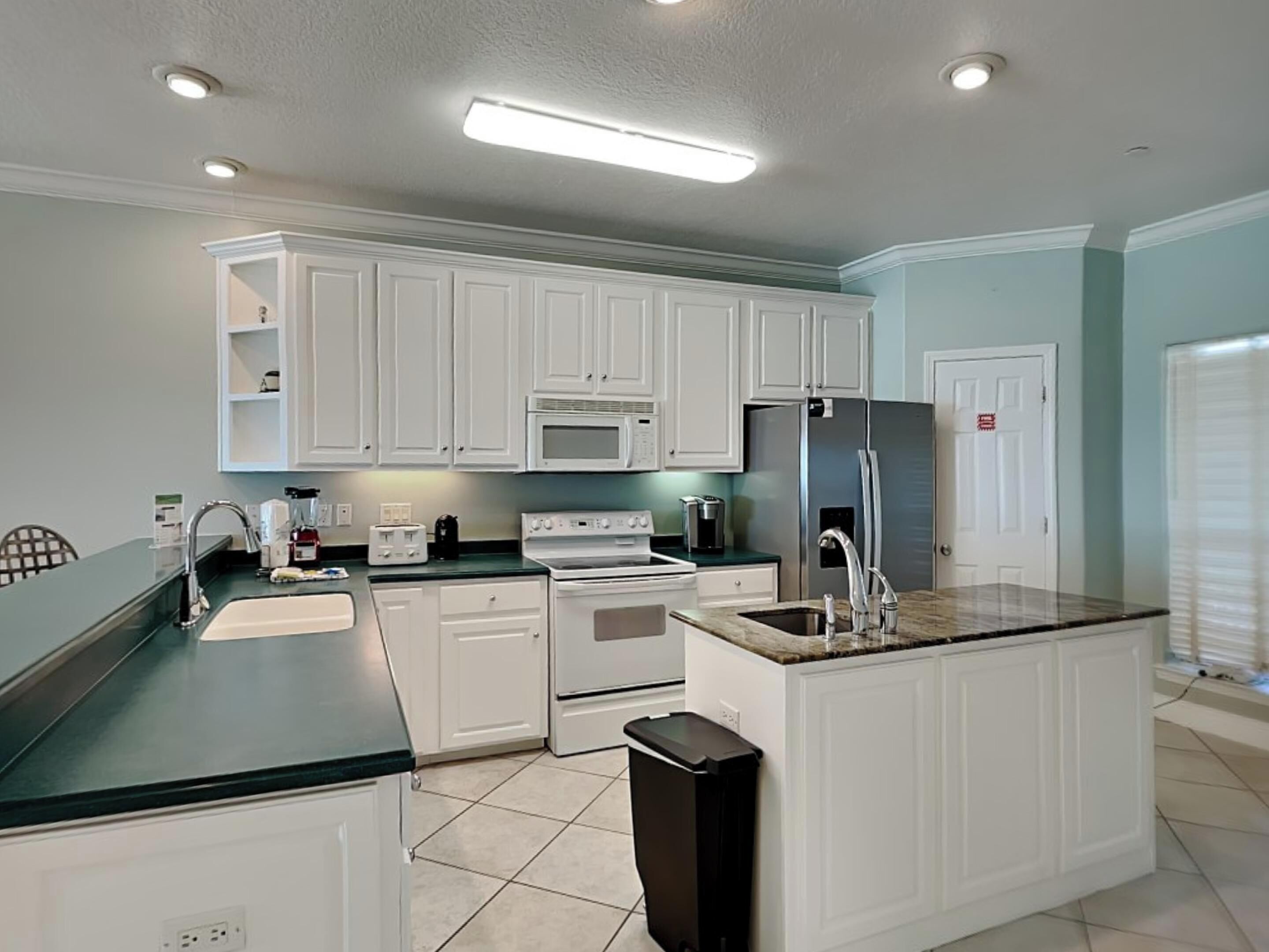 Una cocina moderna con armarios blancos, una isla central, microondas, refrigerador y estufa.