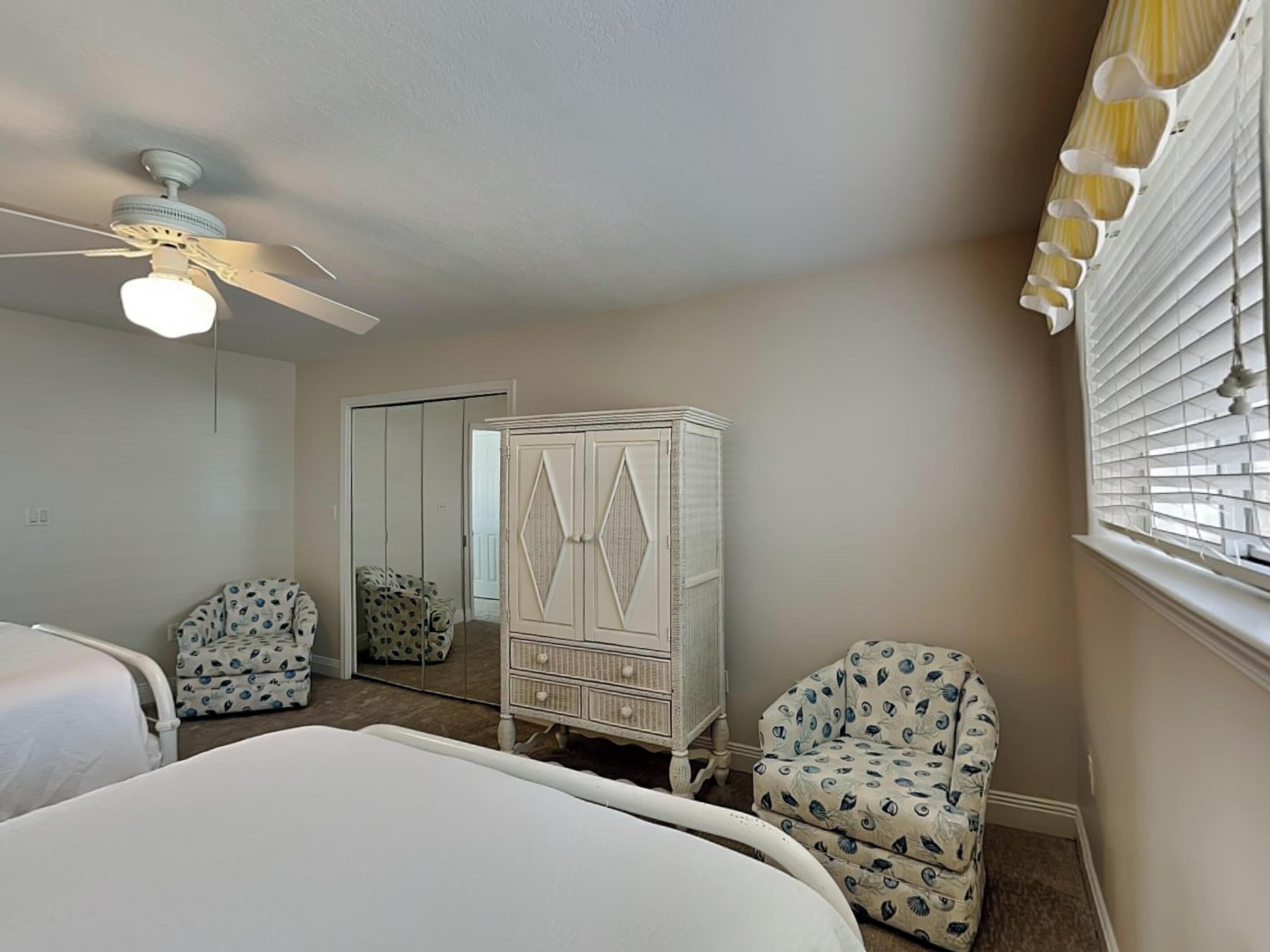 A bedroom with a bed, a white wardrobe, a chair, and a ceiling fan.