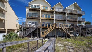 A beachfront hotel with multiple balconies, wooden staircases, and a wooden boardwalk leading to the entrance. - Anchor Townhome #5 by Southern Vacation Rentals (Destin)