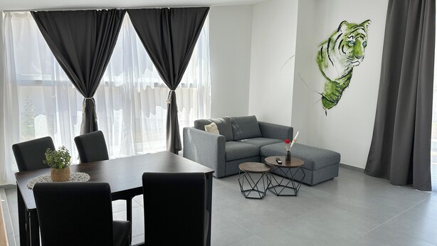 A modern living room with a grey sofa, a dining table with chairs, and a wall-mounted painting of a tiger. - Grazora Living Apartments (Graz)