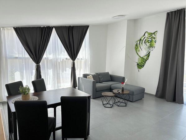 Un salón moderno con un sofá gris, una mesa de comedor con sillas y un cuadro colgado en la pared de un tigre.