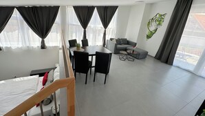 A modern living space with a dining area, a sofa, and a large window with curtains. - Grazora Living Apartments (Graz)