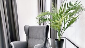 A modern living room with a grey armchair, a glass table, and a potted plant. - Grazora Living Apartments (Graz)