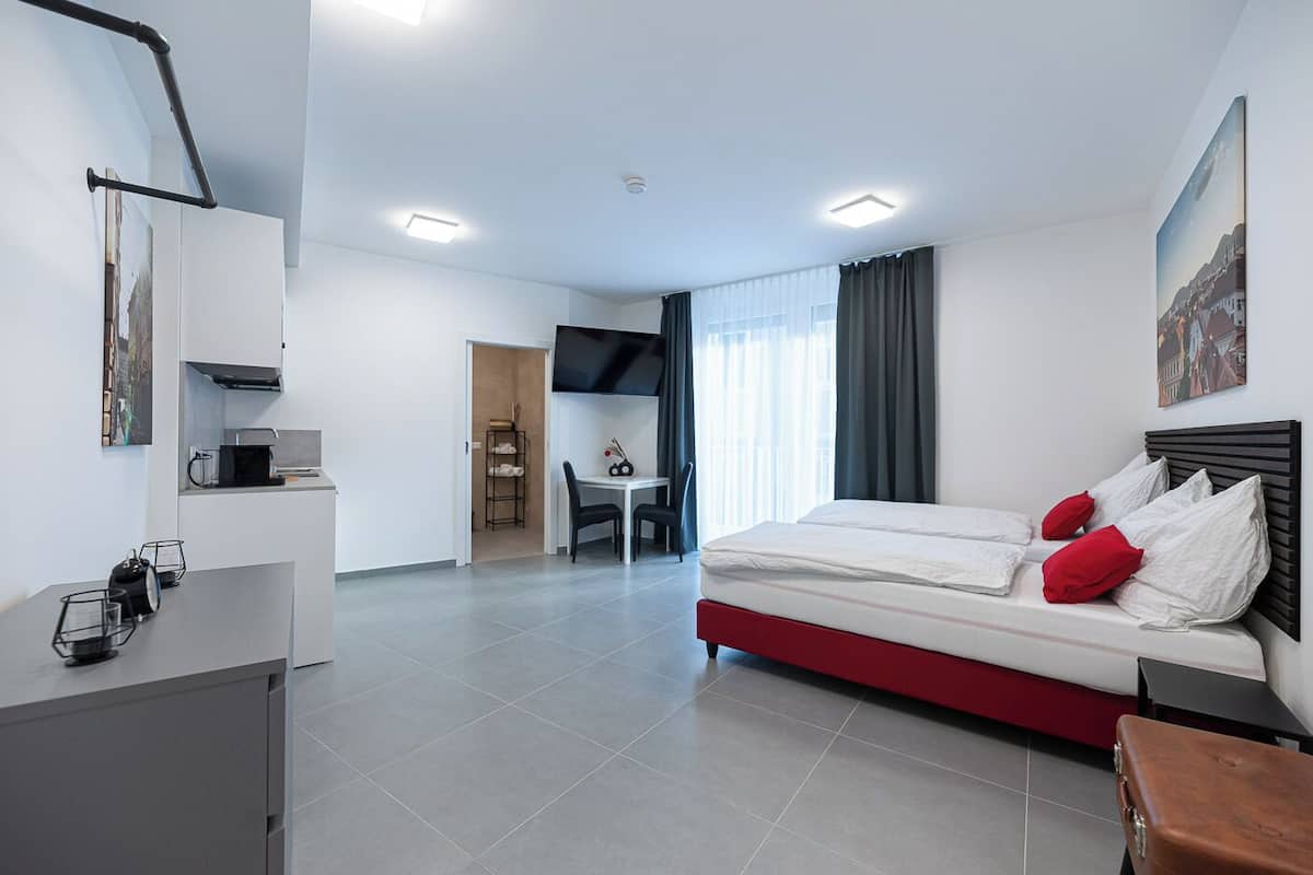 A modern hotel room with a bed, a desk, and a kitchenette.