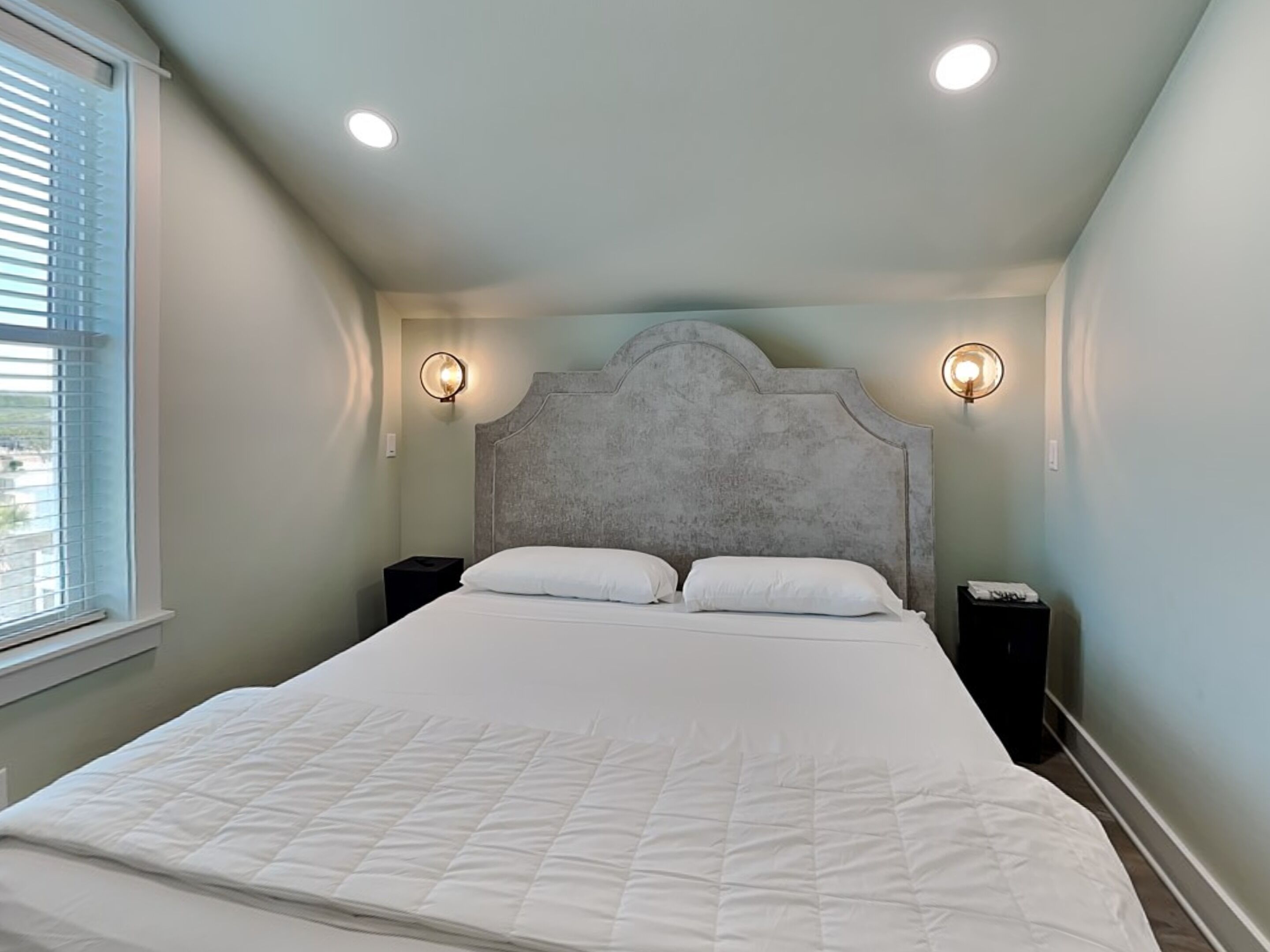 Une chambre à coucher avec un grand lit, deux tables de chevet et deux lampes fixées au mur.