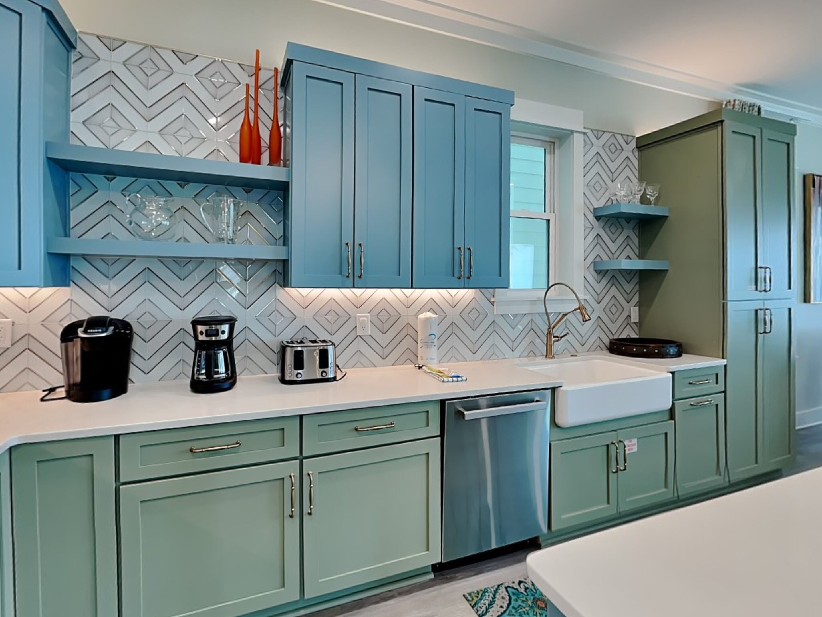 A modern kitchen with teal cabinets, a white countertop, and a patterned backsplash.