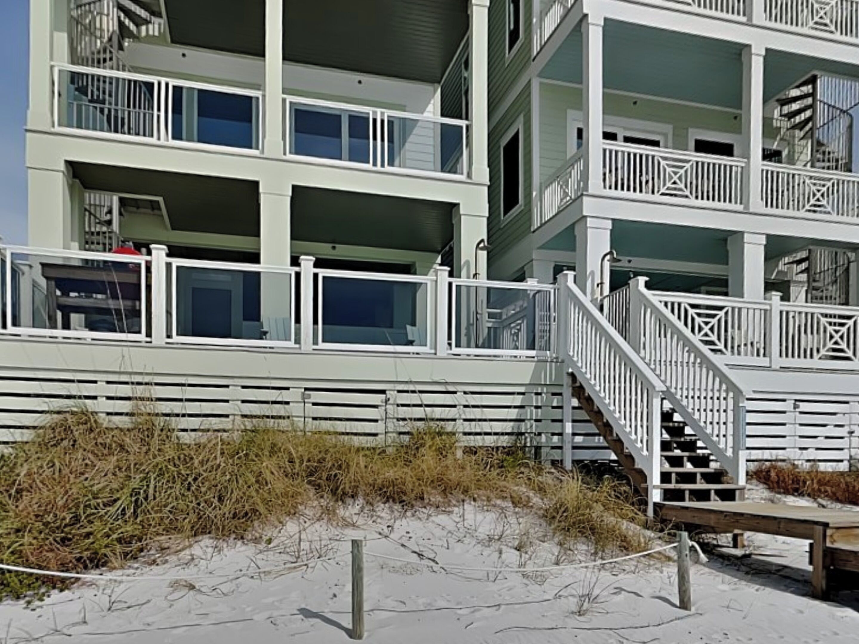 A multi-story beachfront building with balconies, a staircase, and a sandy foreground.