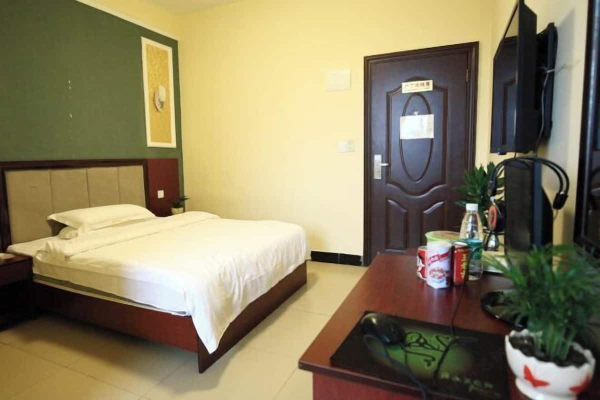 A hotel room with a bed, a desk with a computer, a television, and a door with a sign.