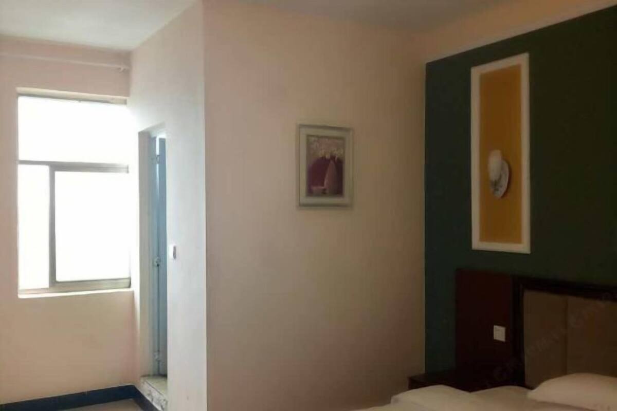 A hotel room with a bed, a small window, and a wall-mounted light fixture.