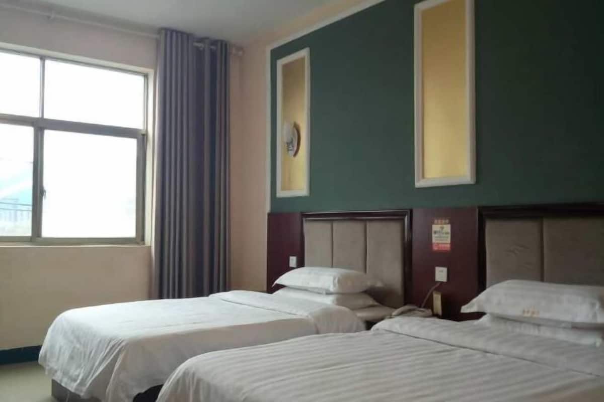 A hotel room with two single beds, a large window with curtains, and a wall-mounted clock.