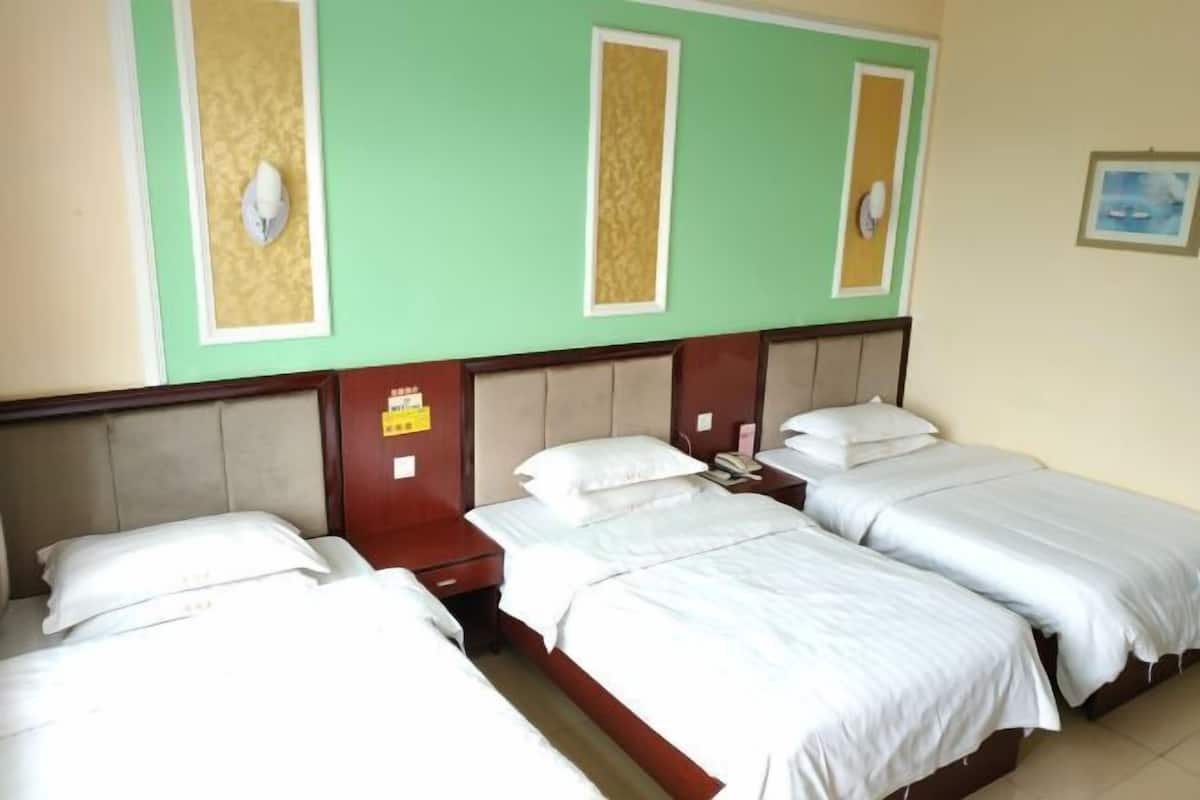 A hotel room with three single beds, a wooden headboard, and a green accent wall.