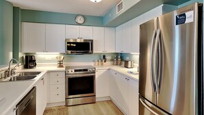 A modern kitchen with white cabinets, stainless steel appliances, a microwave, oven, and refrigerator. - Dune Point #303 by Southern Vacation Rentals (Fort Walton Beach)