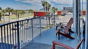 A balcony with a view of a parking lot, palm trees, and a building with a red roof. - Dune Point #303 by Southern Vacation Rentals (Fort Walton Beach)