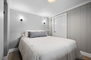 A bedroom with a bed, two wall-mounted lights, a door, and a textured wall.