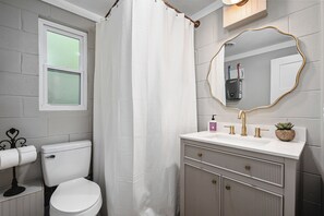 A bathroom with a toilet, a sink with a gold faucet, a mirror with a gold frame, and a shower curtain.