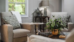 A cozy living room with two armchairs, a small table with a lamp, a birdcage, and a potted plant. - Collins River Cottage (Warren County)