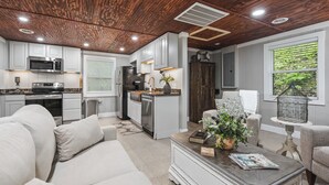 A modern kitchen with white cabinets, a microwave, and a refrigerator. There is a dining area with a white sofa and a coffee table. - Collins River Cottage (Warren County)