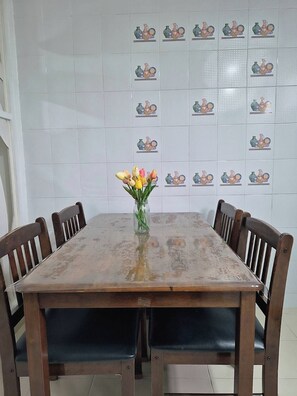 Une table à manger entourée de six chaises en bois, un vase rempli de fleurs et un mur orné de carreaux décoratifs.