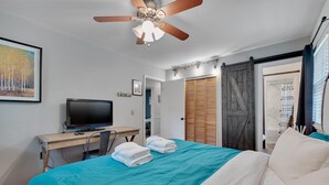 A modern hotel room with a bed, a desk with a computer, a ceiling fan, and a sliding door closet.