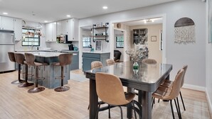 A modern kitchen with a central island, bar stools, and a dining table with chairs.