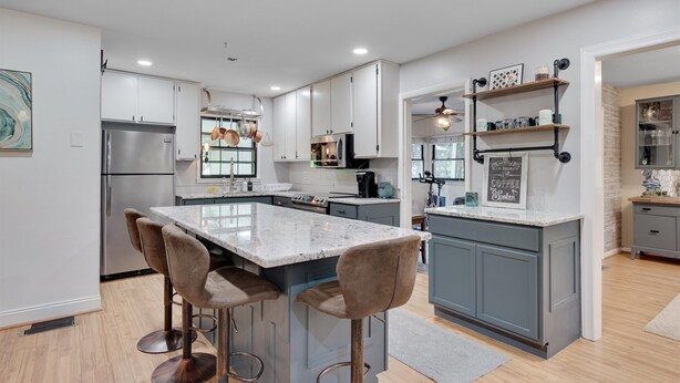A modern kitchen with a central island, bar stools, stainless steel appliances, and a chalkboard menu.