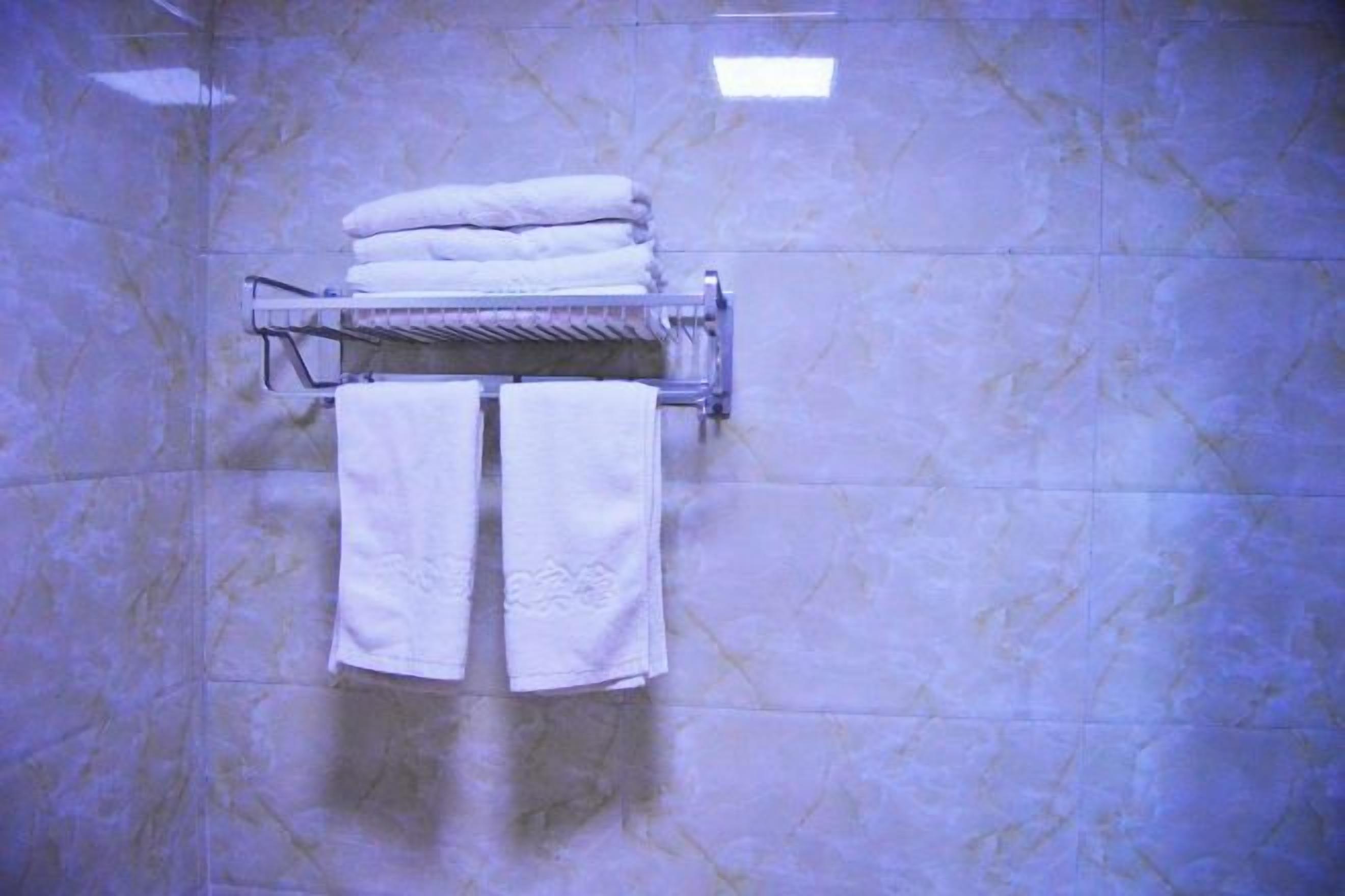 A bathroom with a marble wall, a towel rack with folded towels, and a mirror.