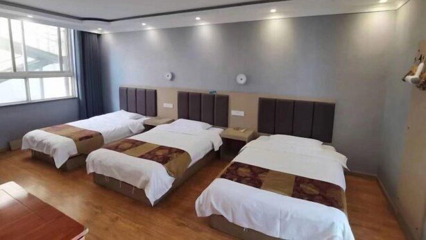 Une chambre d’hôtel avec trois lits simples, un bureau en bois et une grande fenêtre.