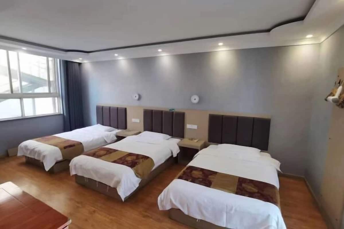 Une chambre d’hôtel avec trois lits simples, un bureau en bois et une grande fenêtre.