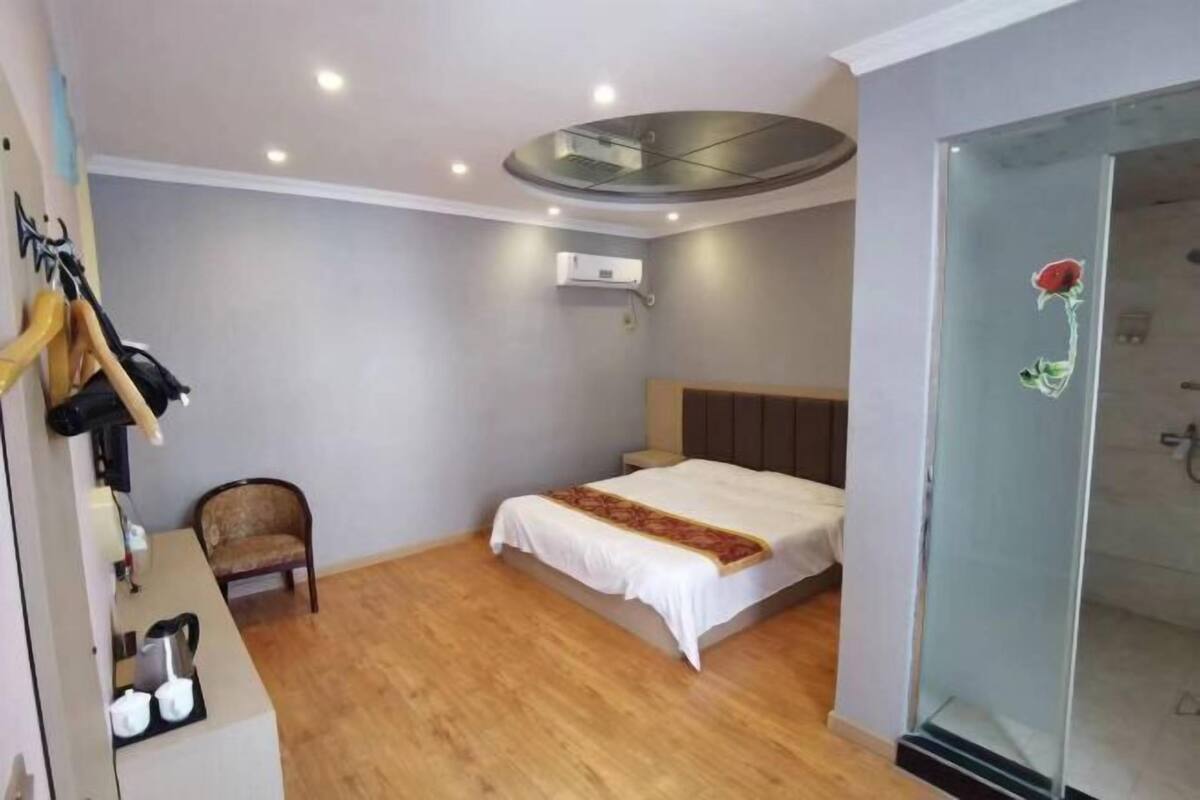 Une chambre comprenant un lit, une chaise, un bureau avec une bouilloire et une douche à parois de verre.