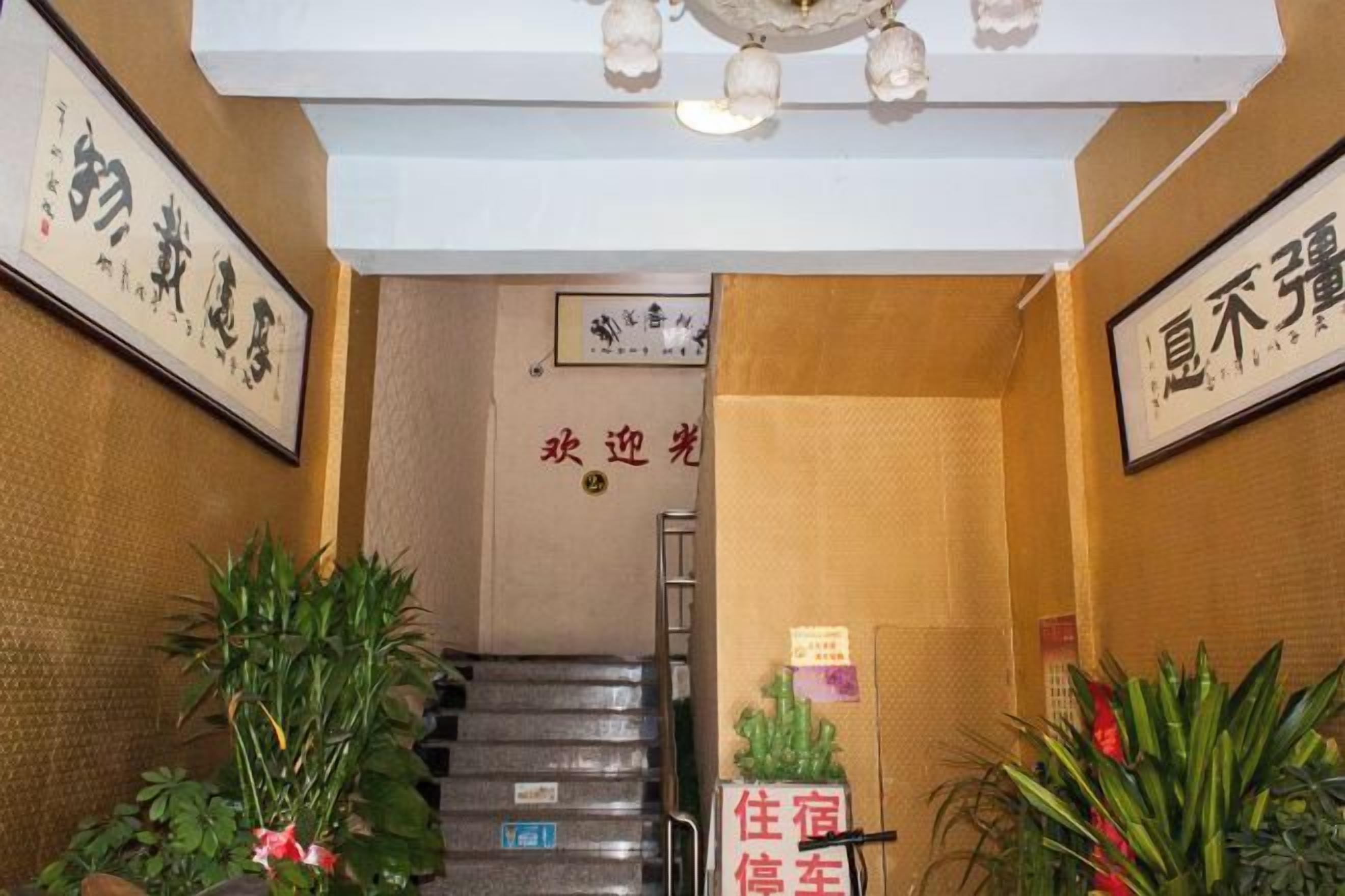 A hotel entrance with a staircase, framed calligraphy, and potted plants.