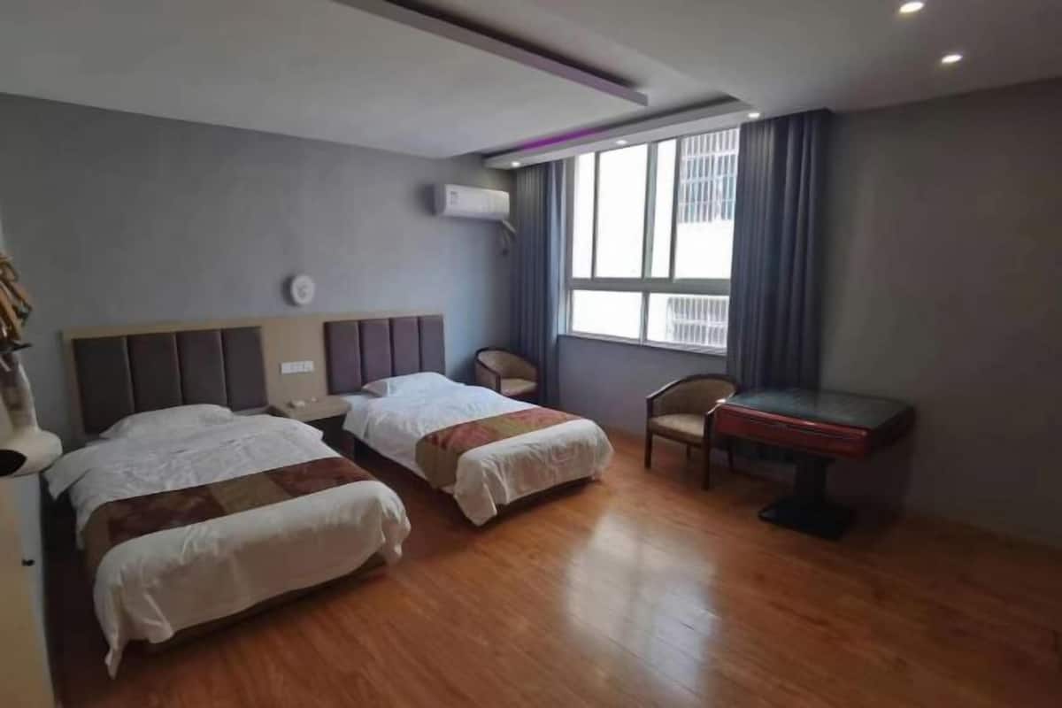 Une chambre d’hôtel avec deux lits, un bureau, une chaise, une fenêtre avec des rideaux et un appareil de climatisation.