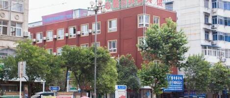 A multi-story building with a red facade, several windows, and a green construction area on the roof.