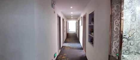 Un pasillo con piso alfombrado, paredes blancas y un papel tapiz estampado a la derecha.