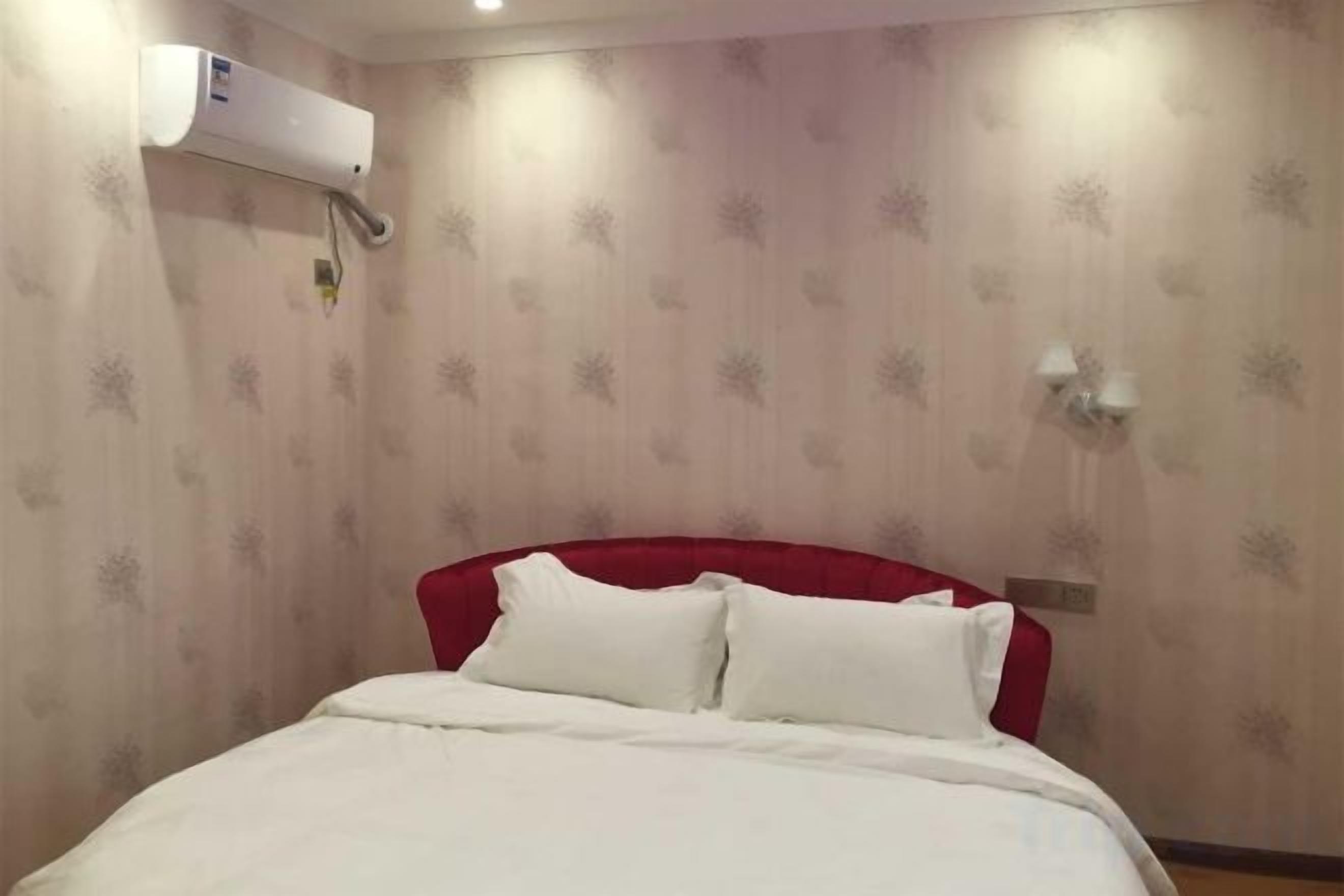 Habitación de hotel con una cama, cabecera roja, aire acondicionado de pared y aplique.