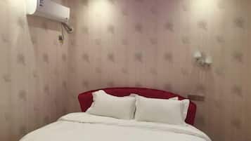 Habitación de hotel con una cama, cabecera roja, aire acondicionado de pared y aplique.
