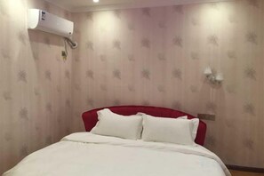 Une chambre d’hôtel avec un lit, une tête de lit rouge, un climatiseur fixé au mur et un applique murale.
