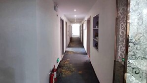 Un long couloir étroit, doté d’un sol recouvert de moquette, de murs blancs et d’un extincteur placé sur le côté gauche.