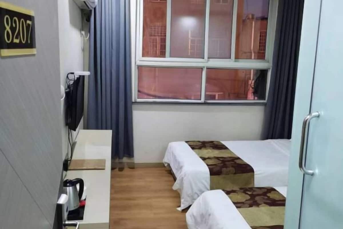 Une chambre avec deux lits, un bureau avec une bouilloire, une télévision et une fenêtre avec des rideaux.