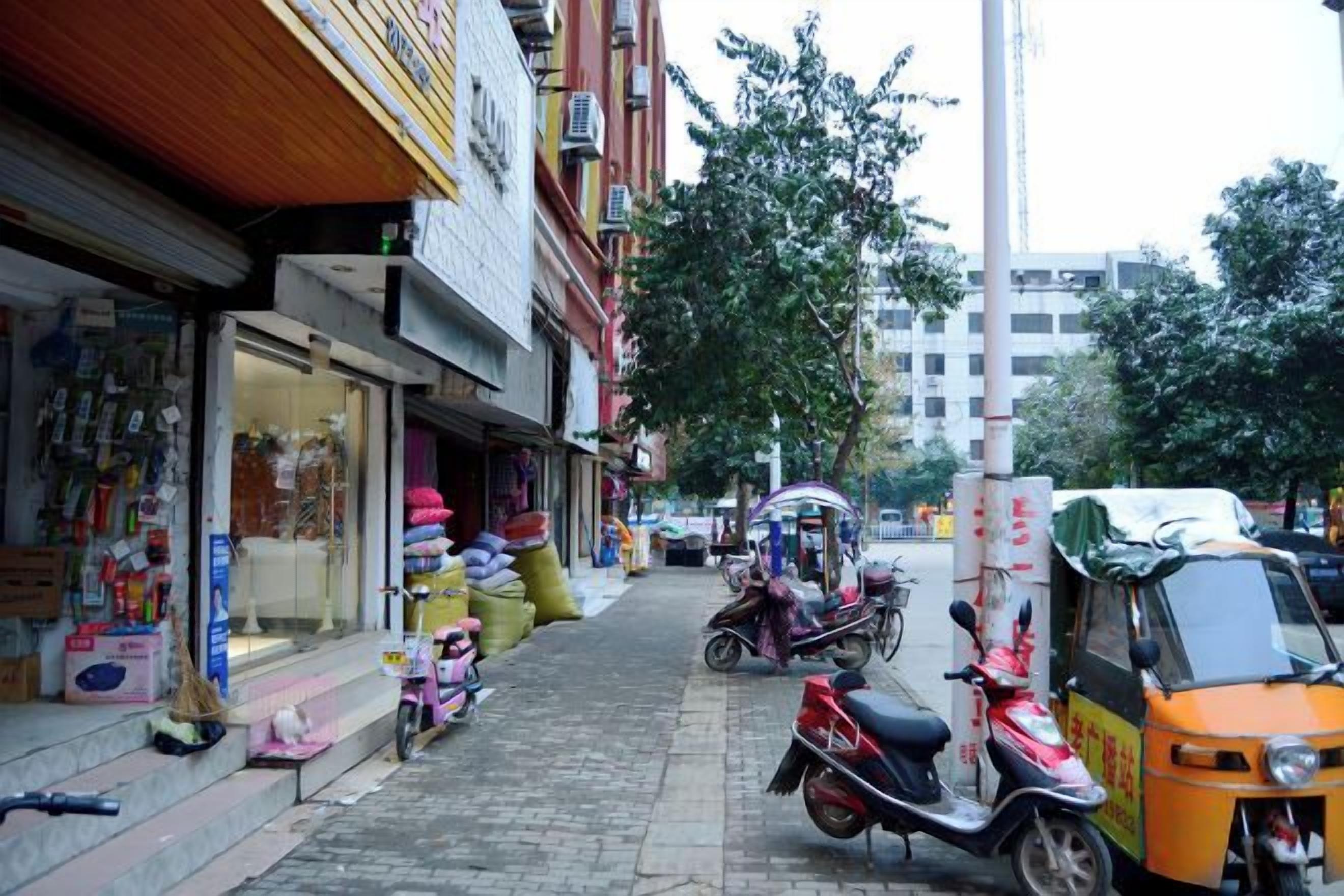 A narrow street with shops on one side and parked vehicles on the other.